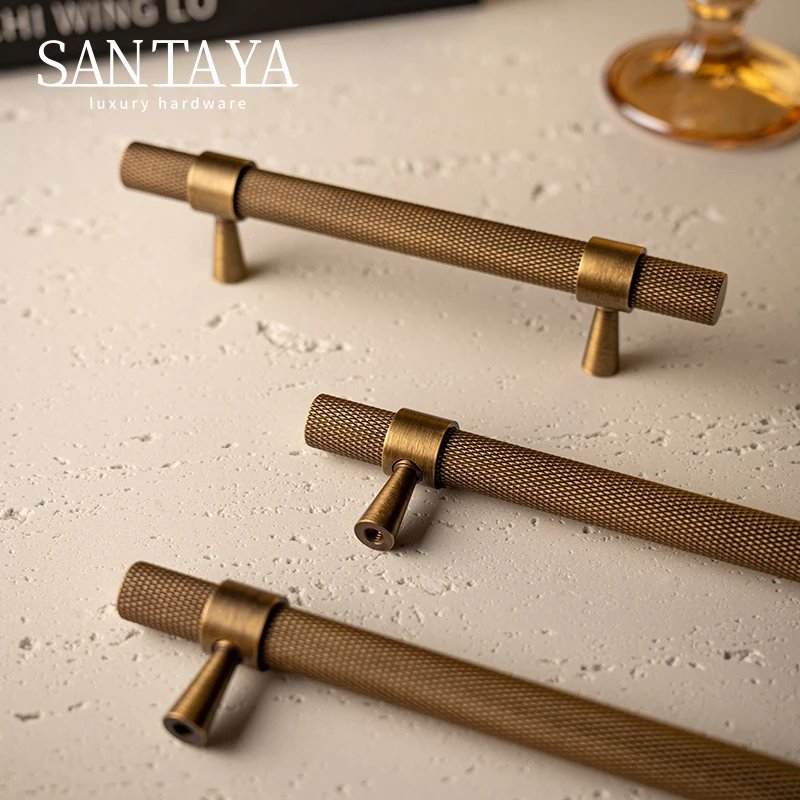 Antique brass bar pulls and T knob arranged on a beige surface