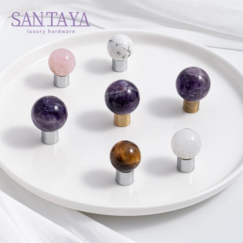 Round crystal and stone furniture knobs in white pink purple and brown on a tray