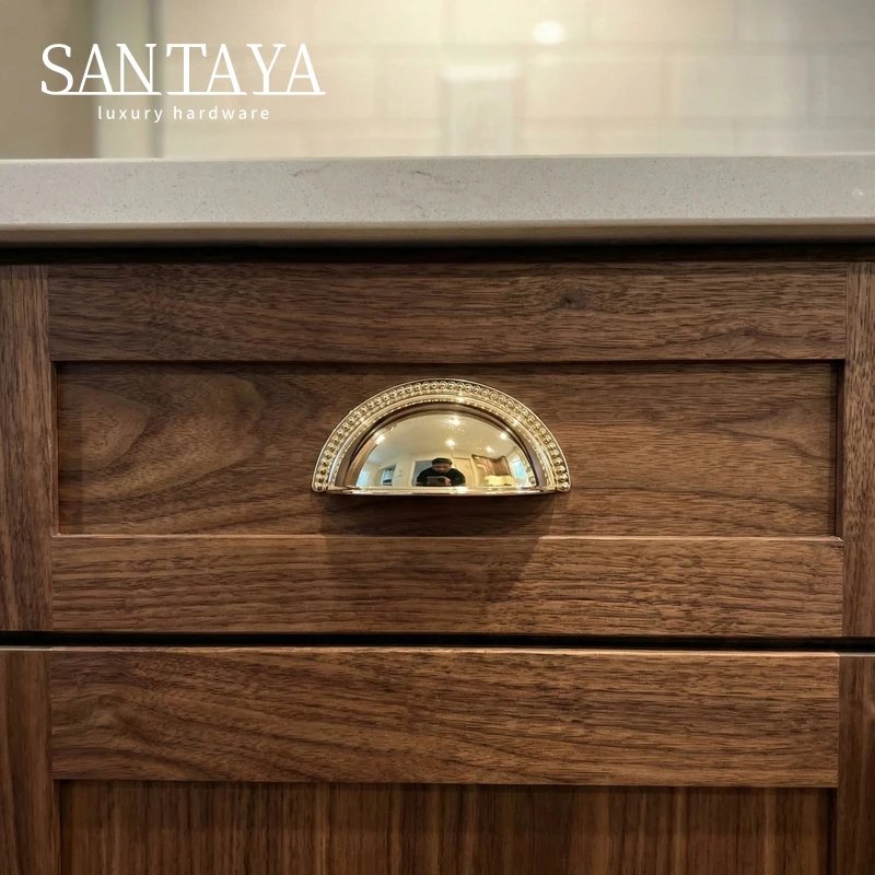 Gold cup pull fitted to a dark wooden drawer front
